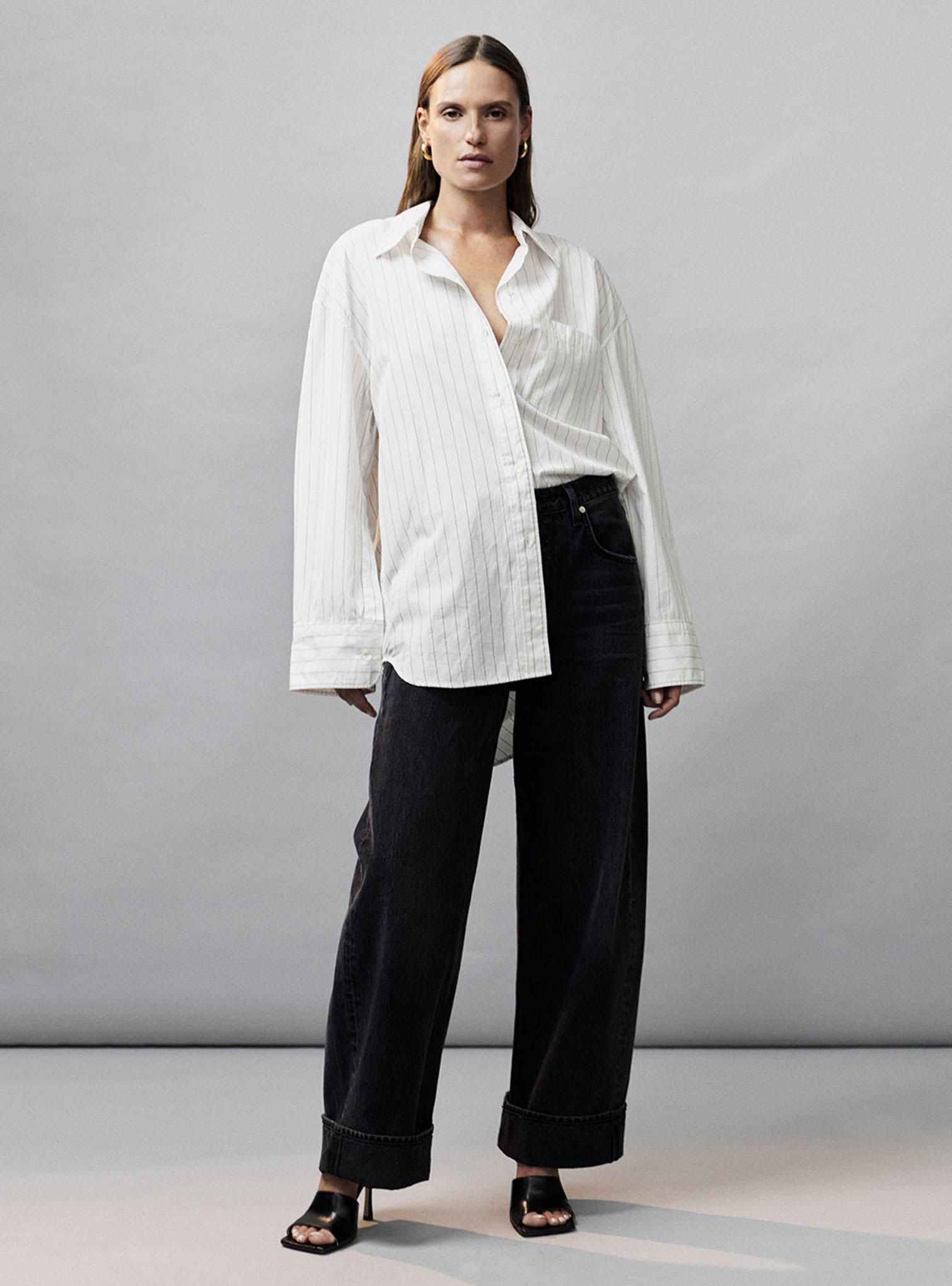 Black wide cuffed denim jeans, black mules, and half tucked white button up shirt with stripes