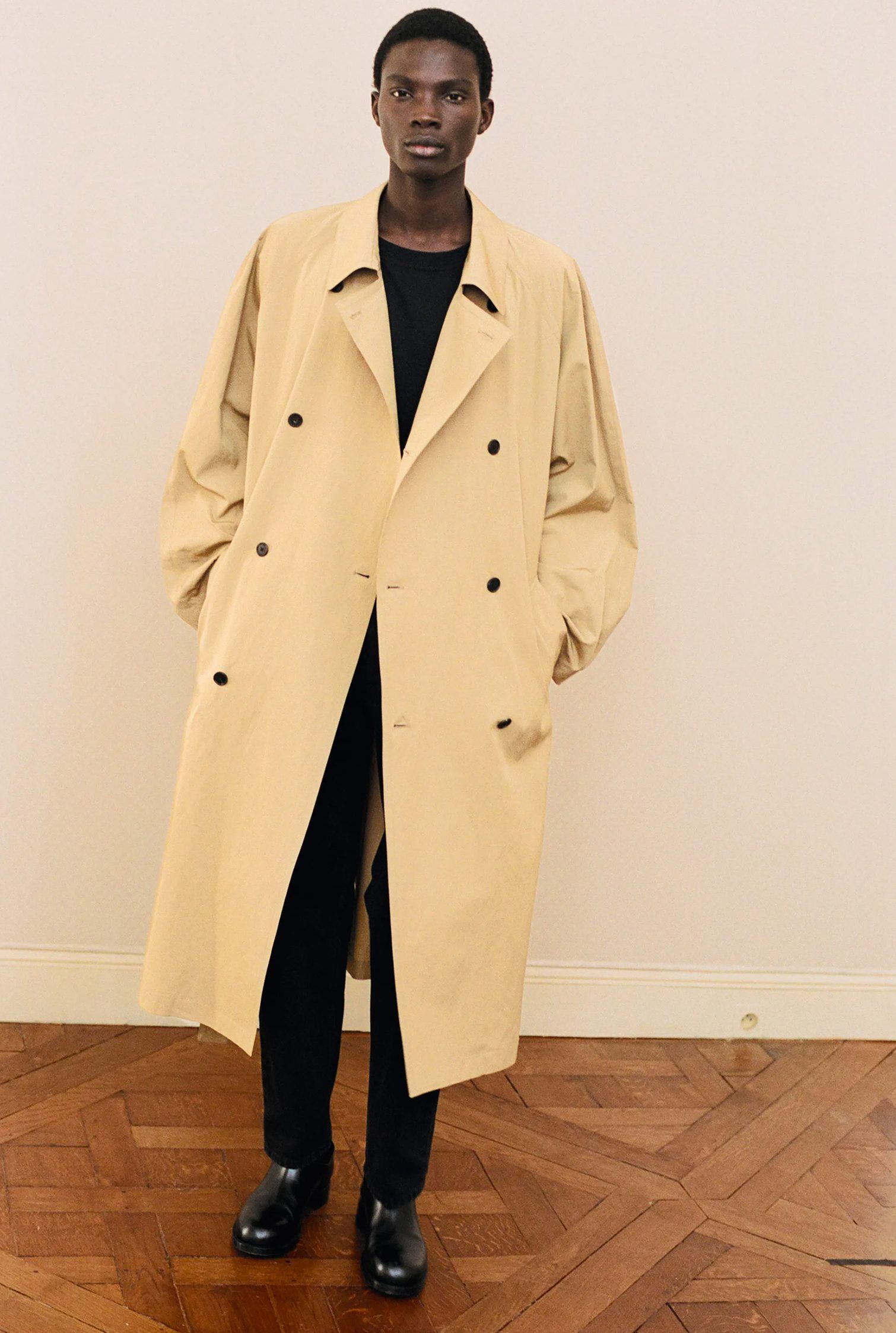The Row total look: model wears a long khaki coat over a black monochrome outfit and black leather boots