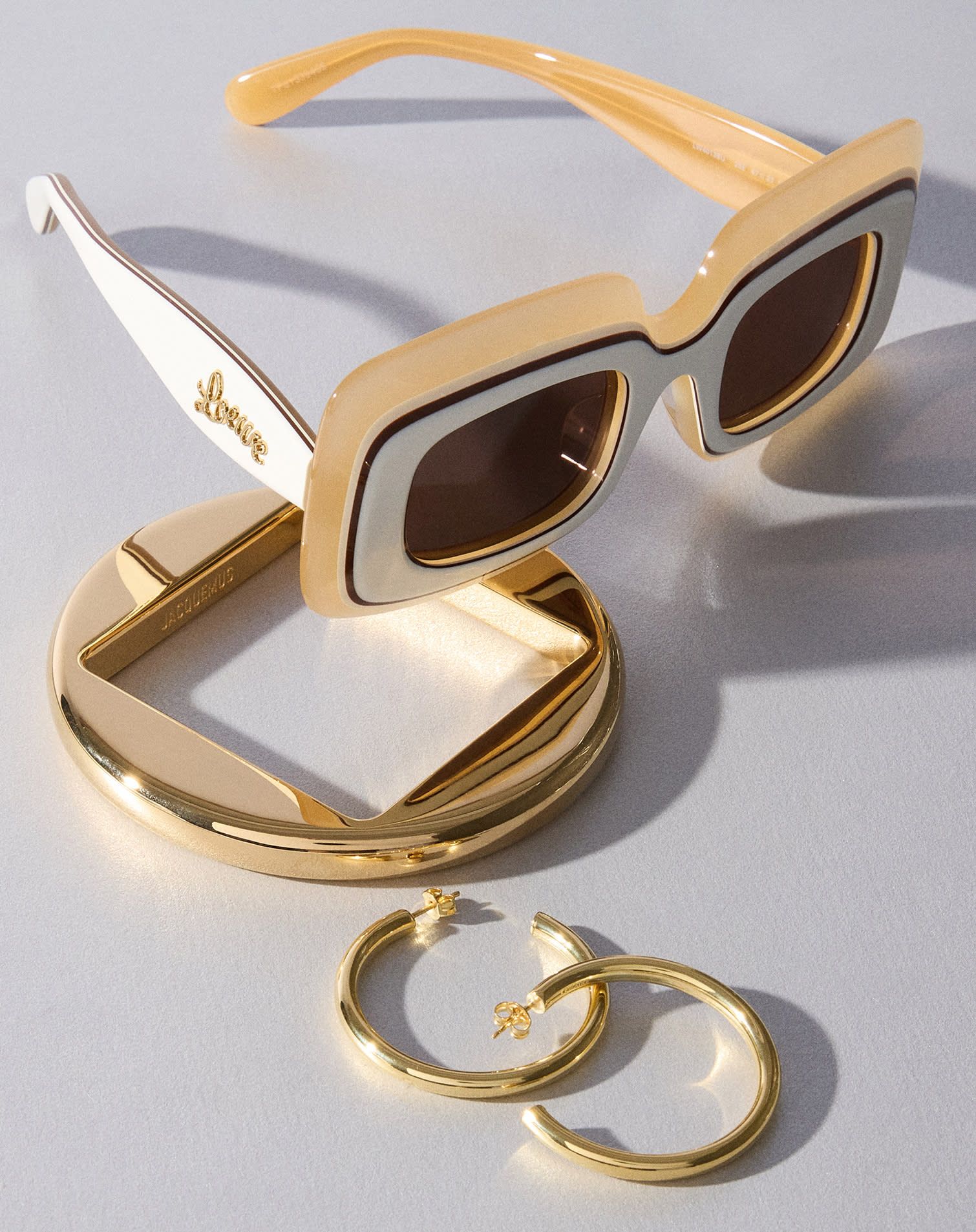 Gold bangle bracelet, gold hoop earrings, and chunky beige and while Loewe sunglasses
