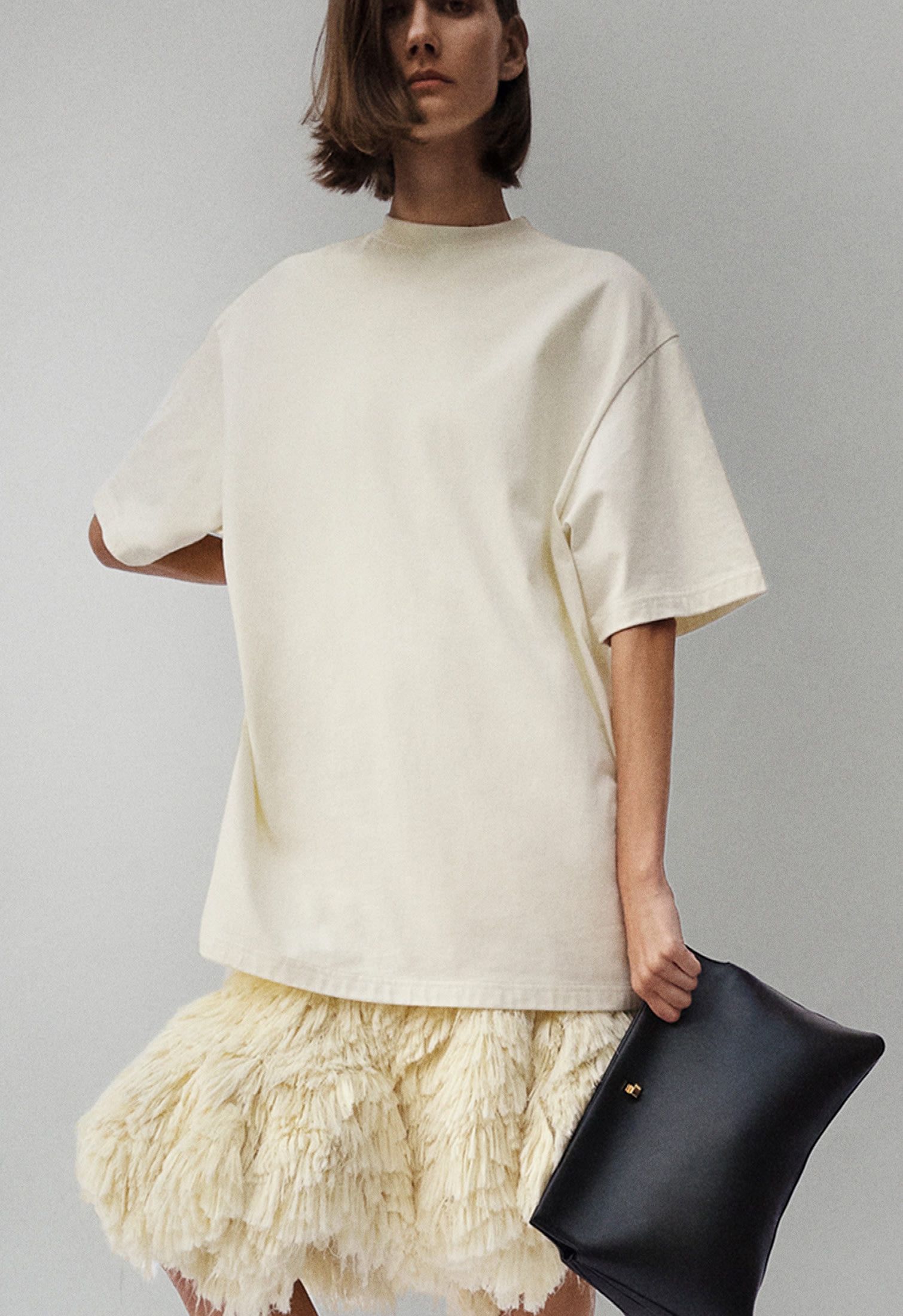 woman wearing an oversized off-white t-shirt, fluffy skirt and black clutch