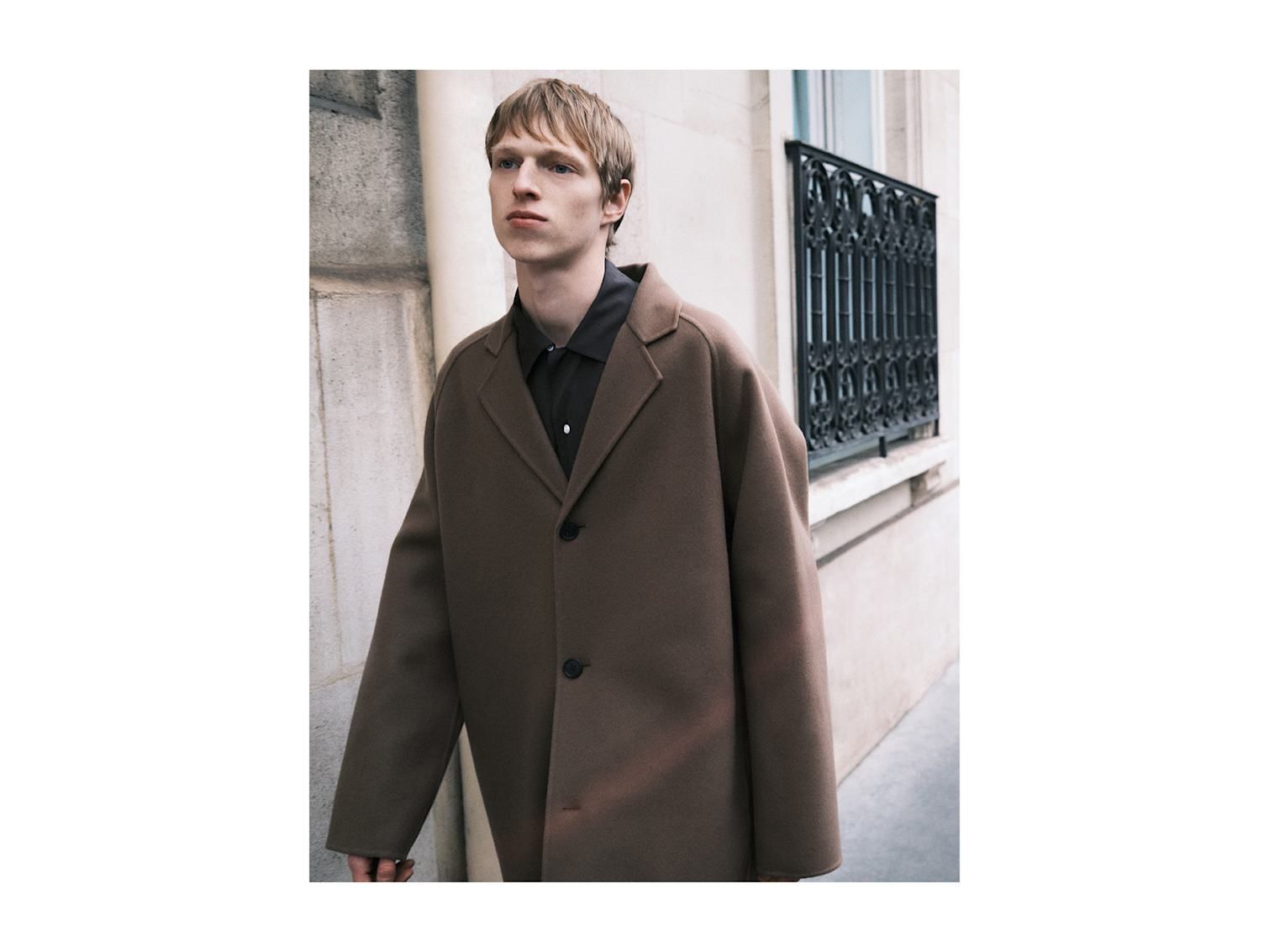 Man wears The Row Moliere wool coat with The Row Anthony cotton shirt.