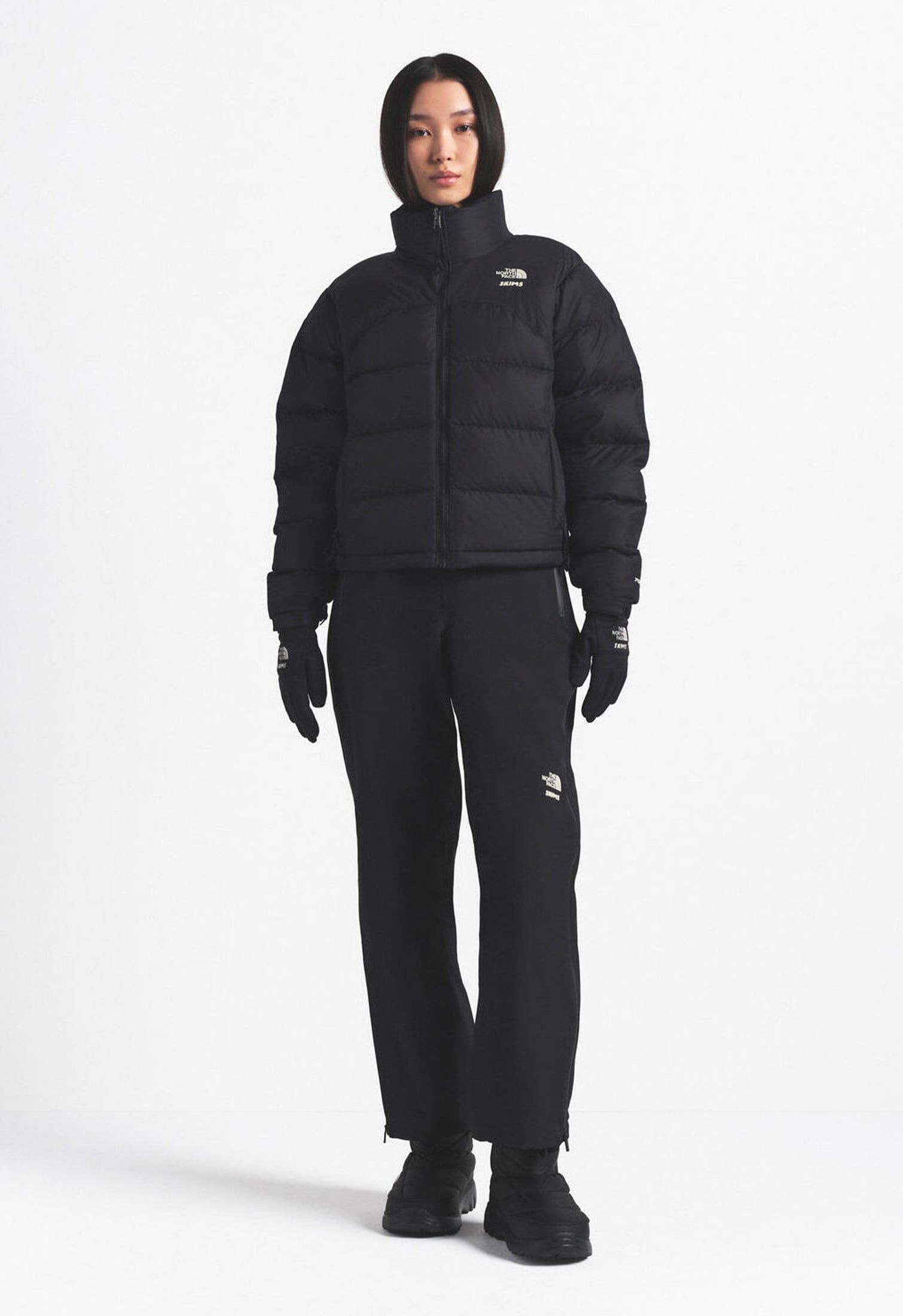 Model with total black outfit: black down jacket, blackgloves, black apres-ski boots and black pants