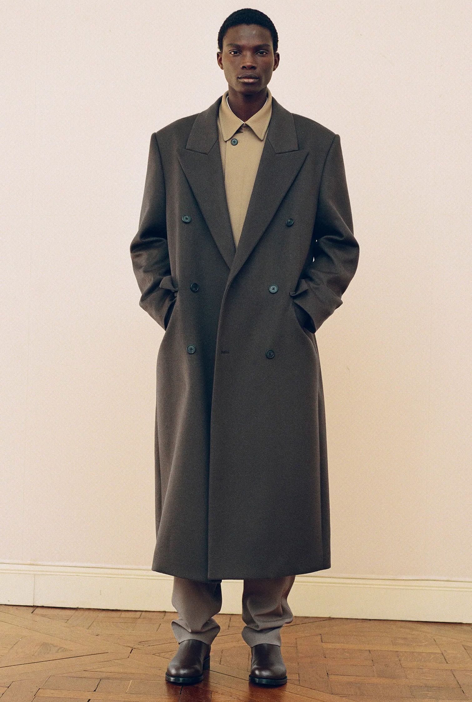 Model wears The Row total look of green cashmere long coat over khaki wool jacket with khaki pants and black boots